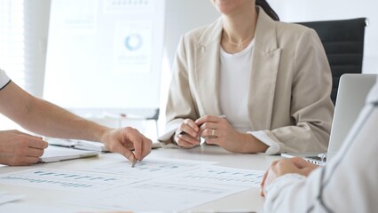 Business team analyzing financial data and discussing marketing strategy during a meeting in the office, businesswoman pointing at charts and explaining strategy to colleagues