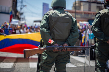A Venezuelan soldier from behind holds a rose, a symbol of violence and peace, next to his weapon. © Amilciar
