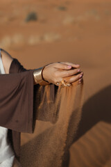 beautiful hands with jewelry are sprinkling fine desert sand