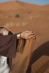 A woman's hands with a beautiful ring, and yellow desert sand spilling from them
