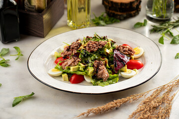 Fresh salad with tuna, cherry tomatoes, avocado, greens, and quail eggs on white plate