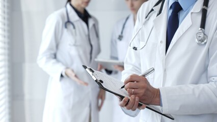 Doctor taking notes on clipboard during discussion with medical team involved in collaborative...