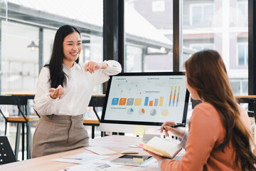 Young businesswoman presenting marketing data with charts and smiling while colleague takes notes in modern office