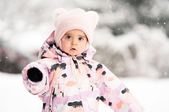 Toddler girl between one and two years old exploring fresh snow outdoors, warm snowsuit and winter hat.
