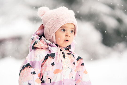 Toddler girl between one and two years old exploring fresh snow outdoors, warm snowsuit and winter hat.