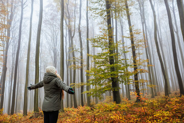Forest bathing. Woman is feeling positive energy in foggy autumn woodland. Mental wellbeing and mindfulness outdoors