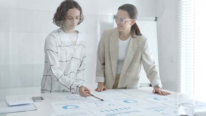 Two businesswomen are examining financial charts and statistics during a productive meeting in a modern office, demonstrating teamwork and strategic planning. Business people concept