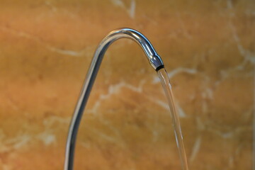 Close-up of Modern Chrome Gooseneck Faucet with a Stream of Clear Running Water Against a Warm Marble-Tiled Background