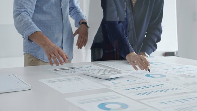 Business professionals analyzing financial charts, gesturing over spreadsheets during collaborative meeting in contemporary workspace, discussing data driven insights
