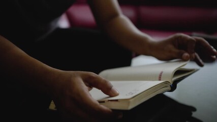 Close up of a man hand opening a diary. Male reading a book while sitting on the sofa in the living room at home.