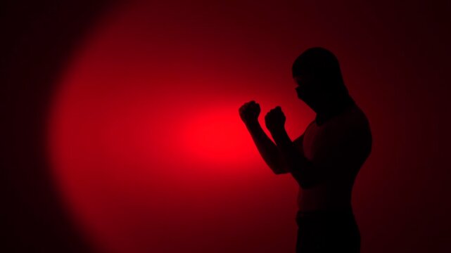 Silhouette man wearing balaclava in aggressive stance, standing in a fighting stance