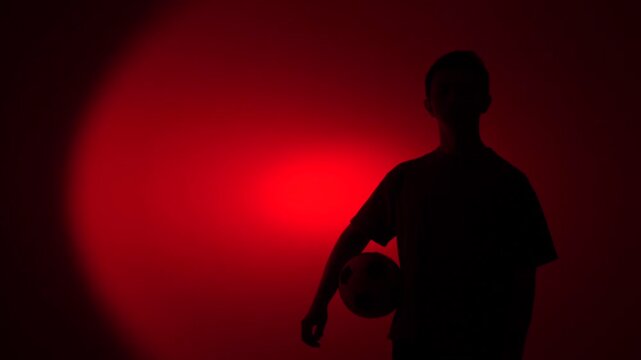 Football player silhouette standing with ball under red spotlight