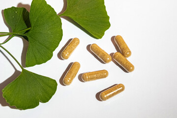 Natural herbal supplement capsules with green ginkgo biloba leaves on a white background. Concept...