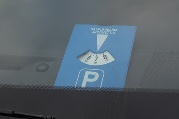 Close-up of a Blue European Parking Disc Displayed on a Car Dashboard Behind the Windshield, Set to 7:00 AM