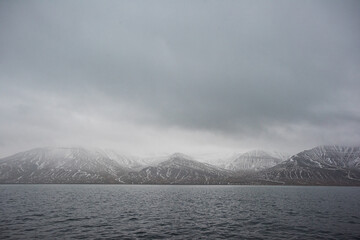 Wide view of snow-covered Arctic mountains across a cold fjord under dramatic gray clouds on Svalbard, Norway.