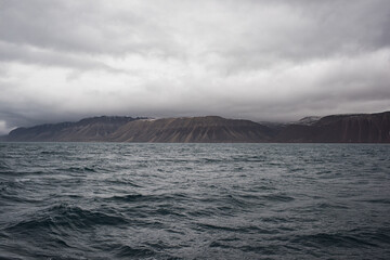 Dark Arctic waters and rugged mountain slopes beneath heavy clouds on Svalbard, Norway, capture the power and solitude of the polar wilderness.