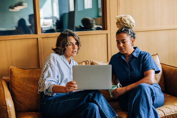 Two women discussing ideas while using a laptop on a comfortable couch