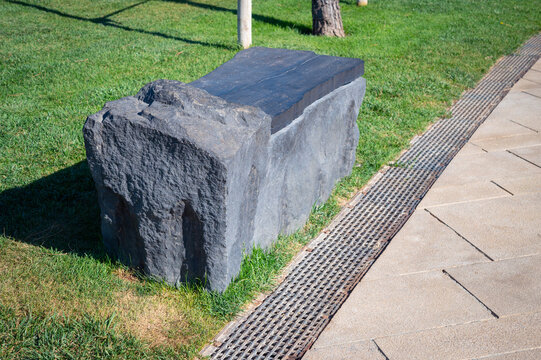 A unique stone park bench on the sidewalk in the park.