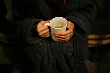 hands holding ceramic cup for warmth with rob in the background and slightly overgrown nails 