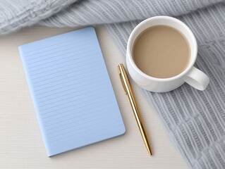 Light blue notebook with lined pages, a golden pen, and a white cup of coffee on a textured gray blanket, creating a cozy workspace atmosphere for creativity and inspiration