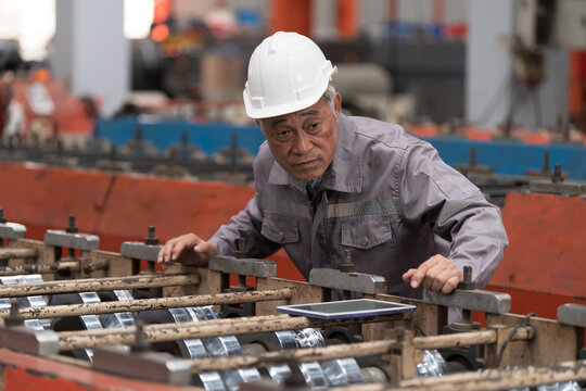 Metalwork manufacturing and factory. Asian senior male engineer checking operation of conveyor for metal sheet during manufacturing process in factory