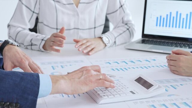 Business people professionals or accouters analyzing financial reports, charts and graphs on laptop and paper, using calculator to discuss strategy, budgeting and teamwork decisions