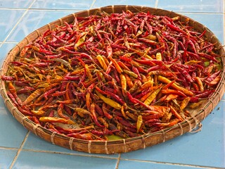 Heap of dried chili peppers arranged on a woven tray, evoking outdoor drying or a market display.