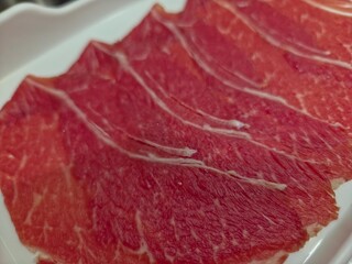 Platter of thinly sliced raw beef brisket, prepared for hot pot dishes such as Shabu-Shabu or Sukiyaki.