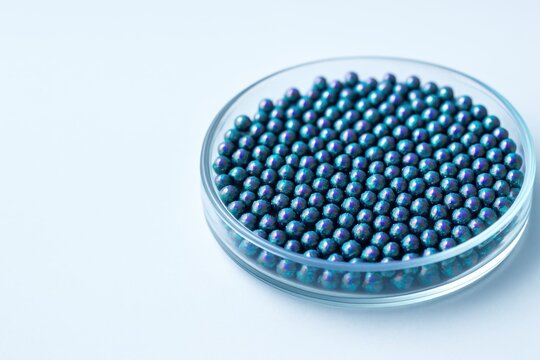 Shiny blue-purple NMC granules in a glass dish under soft light, representing advanced battery material research.