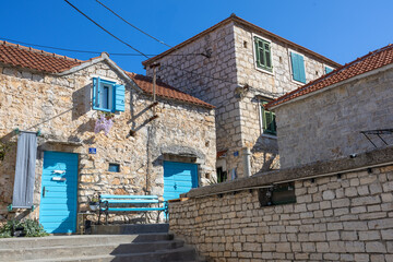 Bright Blue Doors and Shutters Adorn a Rustic Stone House Along a Sunny Mediterranean Street, Maslinica, Croatia