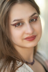 Naklejka premium Young woman with long brown hair and stylish makeup, wearing a cozy knitted cardigan, poses confidently with arms crossed, showcasing a warm and inviting atmosphere