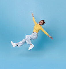 Obraz premium Asian woman floating playfully in mid air isolated on blue background representing freedom happiness energy creativity and positive modern lifestyle