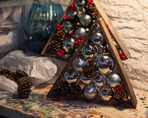 A crafter decorates a wooden tree with ornaments, pinecones, and berries for a festive holiday display.