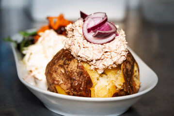 Enjoy a loaded baked potato! A crispy skin holds fluffy potato topped with tuna salad and red onion, served with coleslaw and salad. Yum!