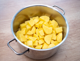 Stainless steel pot filled with peeled and chopped raw potatoes ready for cooking. Freshly prepared potatoes in a kitchen on a wooden surface, home cooking concept.