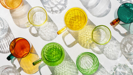 Vibrant of colorful glass cups on white, banner, casting artistic light reflections and shadows in natural sunlight. Summer drink concept, minimal style trend pattern of glasses, diagonal layout