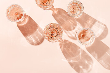 Wine Glasses of rose wine on pink background, sun flare and reflection from sunlight. Aesthetic layout from various crystal glasses, sparkling alcohol drinks, champagne, Summer romantic setting