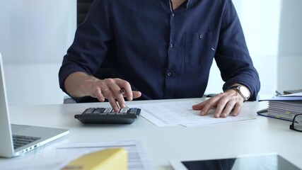Professional businessman calculating financial data, reviewing documents near laptop in modern workplace setting. Audit and taxes, business concept