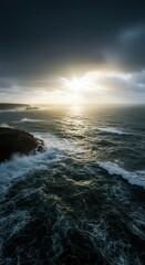 Obraz premium Captivating coastal seascape showcases turbulent waves crashing against rocky cliffs under a dramatic, overcast sky, with a radiant sun breaking through the clouds