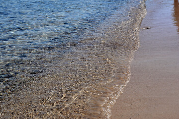 Soft sea wave on the sandy beach. Sea shallows with small pebbles visible on the bottom.