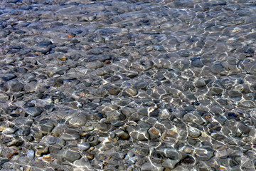 Transparent sea water. Sea water surface background. Sea shallows with visible pebbles at the bottom