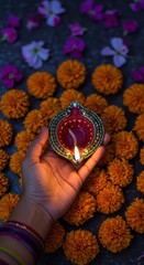 Woman hand holding a lit oil lamp for Diwali celebration. Traditional Indian festival decoration with bright marigold flower and petal arrangement for holiday banner, poster or card.