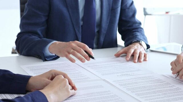 Business people meeting in an office, discussing important documents, pointing to a contract for signature, finalizing a deal, negotiating agreement terms, financial transaction concept