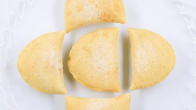 rotating video of frozen mini panzerotti arranged in a circle on a white plate. Italian frozen snack or appetizer concept, close-up of golden dough texture before cooking.