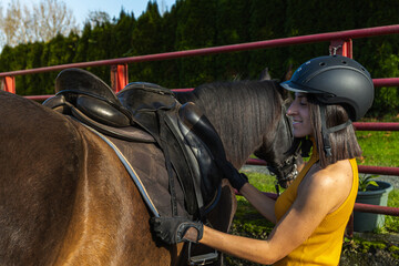 Woman adjusting a saddle on a horse with safety gear. Lifestyle. Horse riding.