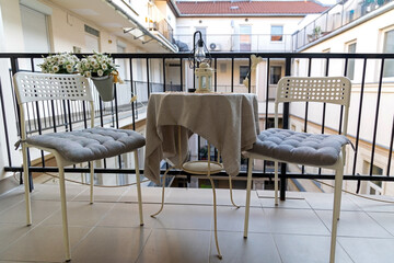 Cozy balcony setting with table and two chairs. Small balcony scene featuring a round table with beige cloth, two white chairs with gray cushions.