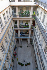 Traditional Apartment Courtyard with Balconies and Flowers. Looking down into a historic residential courtyard lined with wrought iron balconies, potted plants, and tiled walkways in a classic