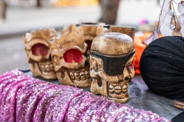 Decorative skulls made of clay in various designs. Colorful fabric draped in the foreground. Scene reflects cultural artistry and craftsmanship.
