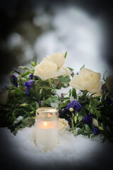 A beautiful memorial bouquet of blue and white flowers on a snowy winter day in a cemetery. Funeral flowers in the winter frost. A flower arrangement on the snowy ground. Dark vignetting.