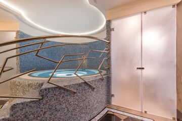 A room in the spa center with a frosted glass door. A small round pool decorated with mosaic tiles.